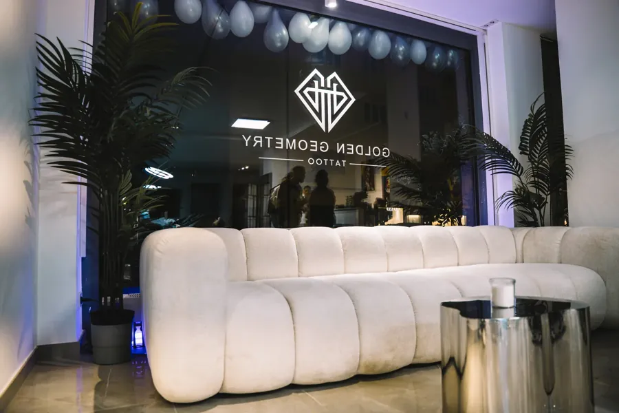 Blick in das Studio Golden Geometry München mit Sofa, Pflanzen und Logo am Fenster